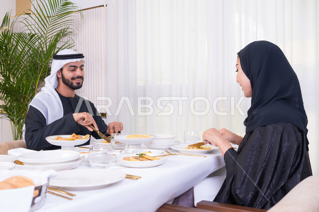 المحبة والألفة والمودة بين الزوجين، الاستمتاع في عطلة نهاية الاسبوع, مائدة مليئة باطباق متنوعه ومختلفه من المأكولات الشهية، زوجان عربيان اماراتيان يقومان بتناول الطعام في المطعم, مفهوم الاسره السعيده