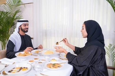 الاستمتاع في عطلة نهاية الاسبوع, مائدة مليئة باطباق متنوعه ومختلفه من المأكولات الشهية، الألفة والمودة بين الزوجين، زوجان عربيان اماراتيان يقومان بتناول الطعام في المطعم, مفهوم الاسره السعيده