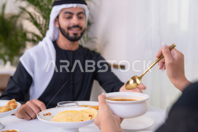 A table full of various delicious dishes, intimacy and affection between spouses, spending a pleasant time outside the home on the weekend, an Emirati Arab couple eating at a restaurant, the concept of a happy family