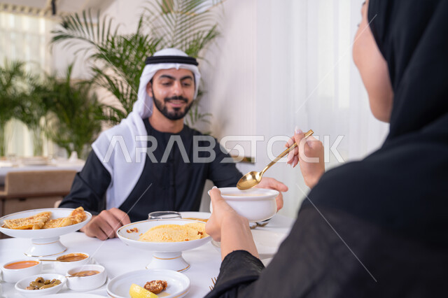 الألفة والمودة بين الزوجين، قضاء وقت ممتعه خارج المنزل في عطلة نهاية الاسبوع, زوجان عربيان اماراتيان يقوم بتناول الطعام في المطعم, مفهوم الاسره السعيده, طاولة مليئة باطباق متنوعه ومختلفه من المأكولات الشهية