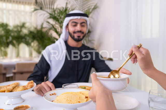 قضاء الأوقات الممتعة في الخارج, إيماءات السعادة و السرور, رجل عربي خليجي إماراتي مبتسم يرتدي الكندورة و الغترة البيضاء يجلس في إحدى المطاعم في الإمارات, أنشطة ترفيهية مسلية, الاستمتاع بالأجواء المميزة في المطعم