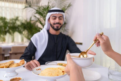 قضاء الأوقات الممتعة في الخارج, إيماءات السعادة و السرور, رجل عربي خليجي إماراتي مبتسم يرتدي الكندورة و الغترة البيضاء يجلس في إحدى المطاعم في الإمارات, أنشطة ترفيهية مسلية, الاستمتاع بالأجواء المميزة في المطعم