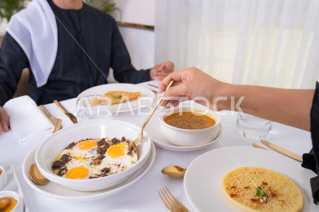 مشاركة الاطعمة بين الزوجين، مائدة مليئة باطباق متنوعه ومختلفه من المأكولات الشهية، الألفة والمودة بين الزوجين، قضاء وقت ممتع خارج المنزل في عطلة نهاية الاسبوع, زوجان عربيان اماراتيان يقومان بتناول الطعام في المطعم, مفهوم الاسره السعيده