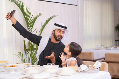 قضاء وقت ممتع خارج المنزل، التسلية والترفيه في العطلة، اب عربي خليجي اماراتي يرتدي الكندورة والغترة يجلس مع ابنته في احدى المطاعم الراقية يقوم بالتقاط صورة تذكارية للحظات السعيدة بتعابير السعادة والسرور