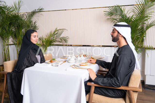 قضاء وقت ممتعه خارج المنزل في عطلة نهاية الاسبوع, مطعم راقي في الامارات العربية المتحدة، زوجان عربيان اماراتيان يقوم بتناول الطعام في المطعم, مفهوم الاسره السعيده, طاولة مليئة باطباق متنوعه ومختلفه من المأكولات الشهية