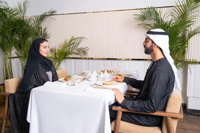 قضاء وقت ممتعه خارج المنزل في عطلة نهاية الاسبوع, مطعم راقي في الامارات العربية المتحدة، زوجان عربيان اماراتيان يقوم بتناول الطعام في المطعم, مفهوم الاسره السعيده, طاولة مليئة باطباق متنوعه ومختلفه من المأكولات الشهية