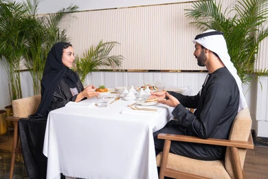 Upscale restaurant in the United Arab Emirates, an Emirati Arab couple eating in the restaurant, the concept of a happy family, spending enjoyable times outside the home on the weekend, a table full of various and different dishes of delicious food