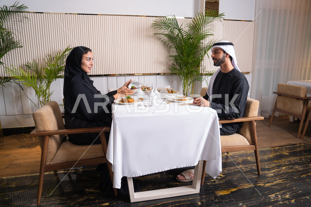 مفهوم المحبة والمودة بين الزوجين، قضاء وقت ممتعه خارج المنزل في عطلة نهاية الاسبوع, مطعم راقي في الامارات العربية المتحدة، زوجان عربيان اماراتيان يقوم بتناول الطعام في المطعم, مفهوم الاسره السعيده, طاولة مليئة باطباق متنوعه ومختلفه من المأكولات الشهية