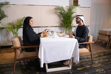 The concept of love and affection between spouses, spending a pleasant time outside the home on the weekend, a high-end restaurant in the United Arab Emirates, an Emirati Arab couple eating at the restaurant, the concept of a happy family, a table full of various and different dishes of delicious food