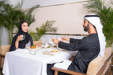 Love and affection between spouses, a high-end restaurant in the United Arab Emirates, a table full of a variety of delicious dishes, spending a pleasant time outside the home on the weekend, an Emirati Arab couple eating at a restaurant, the concept of a happy family