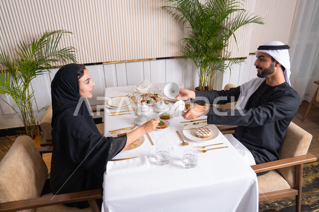 مفهوم المحبة والمودة بين الزوجين، قضاء وقت ممتعه خارج المنزل في عطلة نهاية الاسبوع, مطعم راقي في الامارات العربية المتحدة، زوجان عربيان اماراتيان يقوم بتناول الطعام في المطعم, مفهوم الاسره السعيده, طاولة مليئة باطباق متنوعه ومختلفه من المأكولات الشهية