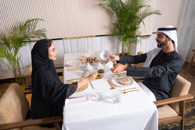 The concept of love and affection between spouses, spending a pleasant time outside the home on the weekend, a high-end restaurant in the United Arab Emirates, an Emirati Arab couple eating at the restaurant, the concept of a happy family, a table full of various and different dishes of delicious food