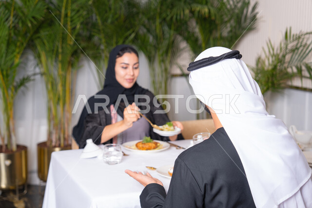 قضاء وقت ممتعه خارج المنزل في عطلة نهاية الاسبوع, مطعم راقي في الامارات العربية المتحدة، زوجان عربيان اماراتيان يقوم بتناول الطعام في المطعم, مفهوم الاسره السعيده, طاولة مليئة باطباق متنوعه ومختلفه من المأكولات الشهية