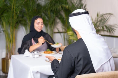 المحبة والمودة بين الزوجين، مطعم راقي في الامارات العربية المتحدة، طاولة مليئة باطباق متنوعه ومختلفه من المأكولات الشهية، قضاء وقت ممتعه خارج المنزل في عطلة نهاية الاسبوع, زوجان عربيان اماراتيان يقوم بتناول الطعام في المطعم, مفهوم الاسره السعيده