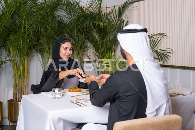 مطعم راقي في الامارات العربية المتحدة، زوجان عربيان اماراتيان يقوم بتناول الطعام في المطعم,, مفهوم الاسره السعيده, قضاء اوقات ممتعه خارج المنزل في عطلة نهاية الاسبوع, طاولة مليئة باطباق متنوعه ومختلفه من المأكولات الشهية