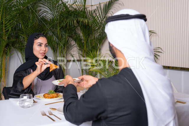 مطعم راقي في الامارات العربية المتحدة، طاولة مليئة باطباق متنوعه ومختلفه من المأكولات الشهية، مفهوم المحبة والمودة بين الزوجين، قضاء وقت ممتعه خارج المنزل في عطلة نهاية الاسبوع, زوجان عربيان اماراتيان يقوم بتناول الطعام في المطعم, مفهوم الاسره السعيده