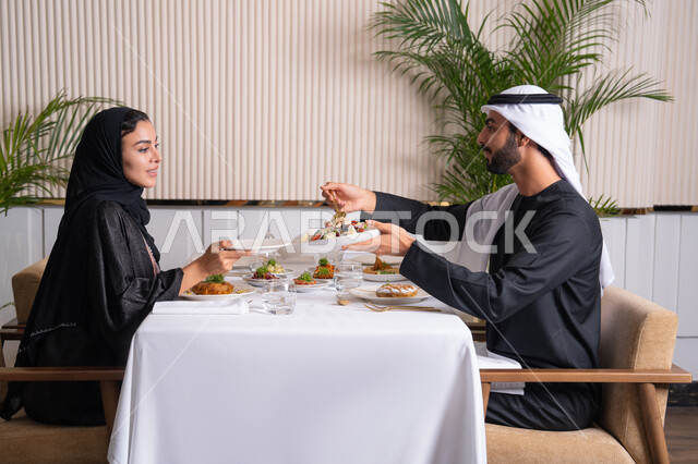 طاولة مليئة باطباق متنوعه ومختلفه من المأكولات الشهية، مفهوم المحبة والمودة بين الزوجين، قضاء وقت ممتعه خارج المنزل في عطلة نهاية الاسبوع, مطعم راقي في الامارات العربية المتحدة، زوجان عربيان اماراتيان يقوم بتناول الطعام في المطعم, مفهوم الاسره السعيده