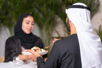 قضاء وقت ممتعه خارج المنزل في عطلة نهاية الاسبوع, مطعم راقي في الامارات العربية المتحدة، زوجان عربيان اماراتيان يقوم بتناول الطعام في المطعم, مفهوم الاسره السعيده, طاولة مليئة باطباق متنوعه ومختلفه من المأكولات الشهية