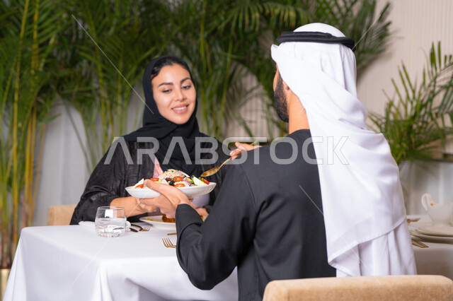مطعم راقي في الامارات العربية المتحدة، زوجان عربيان اماراتيان يقوم بتناول الطعام في المطعم,, مفهوم الاسره السعيده, قضاء اوقات ممتعه خارج المنزل في عطلة نهاية الاسبوع, طاولة مليئة باطباق متنوعه ومختلفه من المأكولات الشهية