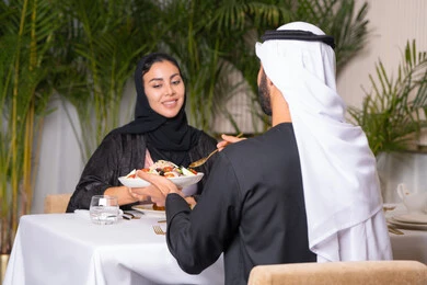 Upscale restaurant in the United Arab Emirates, an Emirati Arab couple eating in the restaurant, the concept of a happy family, spending enjoyable times outside the home on the weekend, a table full of various and different dishes of delicious food