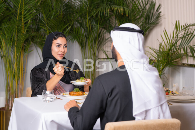 مفهوم المحبة والمودة بين الزوجين، قضاء وقت ممتعه خارج المنزل في عطلة نهاية الاسبوع, مطعم راقي في الامارات العربية المتحدة، زوجان عربيان اماراتيان يقوم بتناول الطعام في المطعم, مفهوم الاسره السعيده, طاولة مليئة باطباق متنوعه ومختلفه من المأكولات الشهية