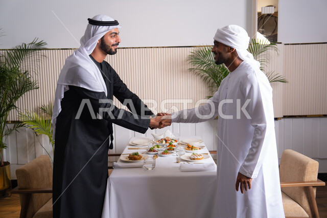 مشاركة الأصدقاء الأوقات الممتعة, بناء علاقات اجتماعية ناجحة, تبادل الأحاديث والاخبار, صديقان عربيان خليجيان اماراتيان يرتديان الزي الاماراتي يقومان بمصافحة بعضهما في إحدى المطاعم في الإمارات