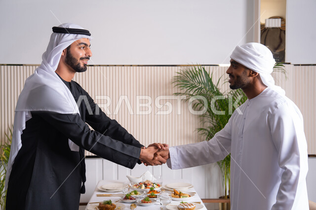 ايماءات السعادة والسرور، مشاركة الأصدقاء الأوقات الممتعة, بناء علاقات اجتماعية ناجحة, تبادل الأحاديث والاخبار, صديقان عربيان خليجيان اماراتيان يرتديان الزي الاماراتي يقومان بمصافحة بعضهما في إحدى المطاعم في الإمارات