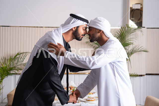 عقد صفقات عمل ناجحة والإتفاق على المشاريع الجديدة، المصافحة بين الأصدقاء في مطعم راقي في الإمارات العربية المتحدة، رجلان أعمال عربيان خليجيان إماراتيان يرتديان الغترة والكندورة الإماراتية ويقومان بقبلة الأنف التقليدية، التحية الإماراتية التقليدية