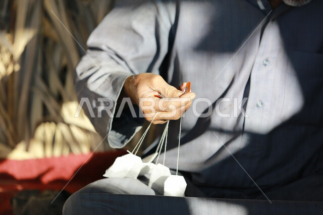 رجل عربي خليجي سعودي يحمل بيده فتلات الشاي ، اعداد وتحضير الشاي على النار ، رحلات برية ، الحياة البرية في المملكة العربية السعودية