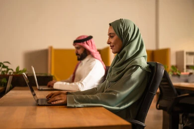 Achieving the company's financial goals, developing projects and investments, studying statistical data papers, managing and dividing tasks, a Saudi Gulf Arab team conducting a business meeting in the company's conference room, integrating modern technological devices into office work.