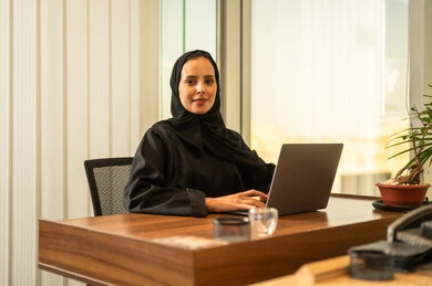 مهن ووظائف نسائية، مفهوم خدمة العملاء، دمج العمل مع التقنية والتكنولوجيا, موظفة عربية خليجية سعودية تجلس على كرسي مريح ترتدي الحجاب والعباءة السوداء يقوم بانهاء المهام اليومسة في مكتب شركة شعودية،بيئة عمل مريحة في الشركات والمكاتب