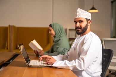 A side view of the camera, focus and meticulous work, dialogues and discussions within the team, business and company development, a work meeting and project completion, discussing plans and explaining work tasks, Arab Omani Gulf colleagues in a meeting, wearing traditional Omani attire.