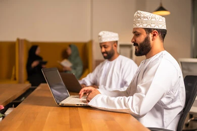 إرسال بريد الكتاروني عبر الحاسوب, استخدام التقنيات الحديثة و المتطورة في العمل, مهن و أعمال مكتبية في سلطنة عمان, رجل عربي خليجي عماني الزي الثوب التقليدي يجلس داخل المكتب و يقوم باستخدام اللابتوب المحمول, التواصل مع العملاء عن بعد