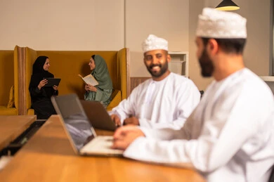 مهن و أعمال مكتبية في سلطنة عمان, إرسال بريد الكتاروني عبر الحاسوب, استخدام التقنيات الحديثة و المتطورة في العمل, رجل عربي خليجي عماني الزي الثوب التقليدي يجلس داخل المكتب و يقوم باستخدام اللابتوب المحمول, التواصل مع العملاء عن بعد