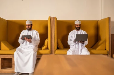 Designated spaces for each employee in the company, focus and meticulous work, dialogues and discussions within the team, business and company development, work meetings and project completion, discussing plans and explaining work tasks, Arab Omani Gulf colleagues in a meeting, wearing traditional Omani attire.
