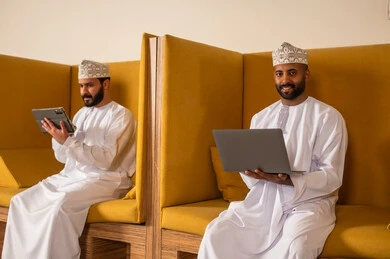إرسال بريد الكتاروني عبر الحاسوب, استخدام التقنيات الحديثة و المتطورة في العمل, مهن و أعمال مكتبية في سلطنة عمان, رجل عربي خليجي عماني الزي الثوب التقليدي يجلس داخل المكتب و يقوم باستخدام اللابتوب المحمول, التواصل مع العملاء عن بعد