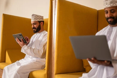 مهن و أعمال مكتبية في سلطنة عمان, إرسال بريد الكتاروني عبر الحاسوب, استخدام التقنيات الحديثة و المتطورة في العمل, رجل عربي خليجي عماني الزي الثوب التقليدي يجلس داخل المكتب و يقوم باستخدام اللابتوب المحمول, التواصل مع العملاء عن بعد
