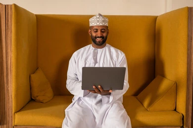 Online video call to accomplish projects, working in Omani offices and companies, focus and meticulous work, dialogues and discussions within the team, business and company development, discussing plans and explaining work tasks, an Arab Gulf Omani employee within an Omani company, wearing traditional Omani attire.