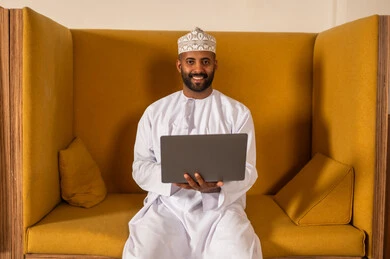 Focus and meticulous work, online video call to accomplish projects, working in Omani offices and companies, dialogues and discussions within the team, business and company development, discussing plans and explaining work tasks, an Arab Gulf Omani employee within an Omani company, wearing traditional Omani attire.