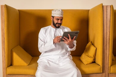 Wearing traditional Omani dress, focus and meticulous work, online video calls to accomplish projects, working in Omani offices and companies, dialogues and discussions within the team, business and company development, discussing plans and explaining work tasks, an Arab Gulf Omani employee within an Omani company.