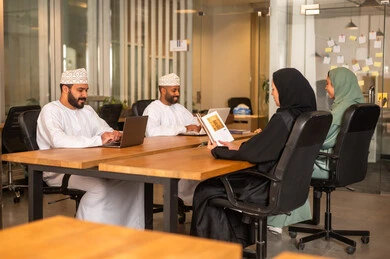 Integrating technology in business and company development, a work meeting to accomplish projects, dialogues and discussions within the team, discussing plans and explaining work tasks, Arab Omani Gulf colleagues in a meeting, wearing traditional Omani attire.