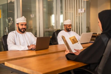 Integrating technology in business and company development, a work meeting to accomplish projects, dialogues and discussions within the team, discussing plans and explaining work tasks, Arab Omani Gulf colleagues in a meeting, wearing traditional Omani attire.