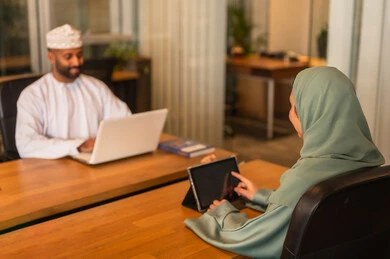 مفهوم التحاور وتبادل الأراء في خطط إنجاز الأعمال، مهن ووظائف إدارية مكتبية في الإمارات،إجراء مقابلة التعيين والتوظيف، مدير عربي خلجي عماني يرتدي الدشداشة و الكمه  داخل المكتب يقوم بإجراء مقابلة عمل مع موظفة، المساواة بين المرأة والرجل