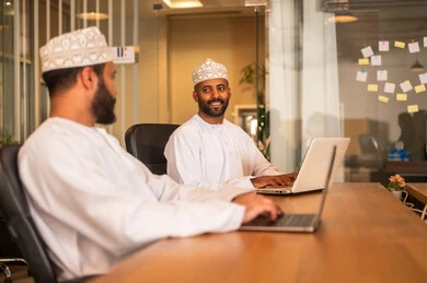 Working in Omani offices and companies, focus and meticulous work, dialogues and discussions within the team, business and company development, work meetings and project completion, discussing plans and explaining work tasks, Arab Omani Gulf colleagues in a meeting, wearing traditional Omani attire.