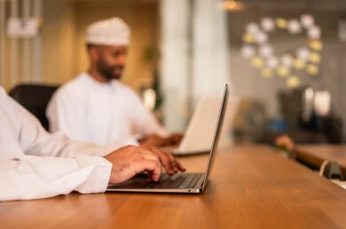 إرسال بريد الكتاروني عبر الحاسوب, استخدام التقنيات الحديثة و المتطورة في العمل, مهن و أعمال مكتبية في سلطنة عمان, رجل عربي خليجي عماني الزي الثوب التقليدي يجلس داخل المكتب و يقوم باستخدام اللابتوب المحمول, التواصل مع العملاء عن بعد