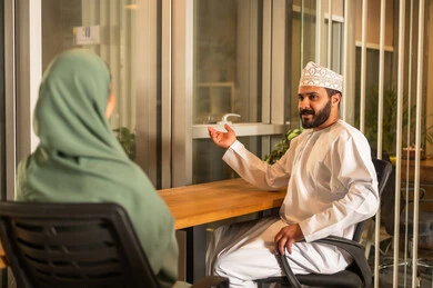 مفهوم التحاور وتبادل الأراء في خطط إنجاز الأعمال، مهن ووظائف إدارية مكتبية في الإمارات،إجراء مقابلة التعيين والتوظيف، مدير عربي خلجي عماني يرتدي الدشداشة و الكمه  داخل المكتب يقوم بإجراء مقابلة عمل مع موظفة، المساواة بين المرأة والرجل