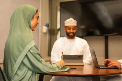 Business and company development, business meeting and project completion, focus and meticulous work, dialogues and discussions within the team, discussing plans and explaining work tasks, Arab Omani Gulf colleagues in a meeting, wearing traditional Omani attire.
