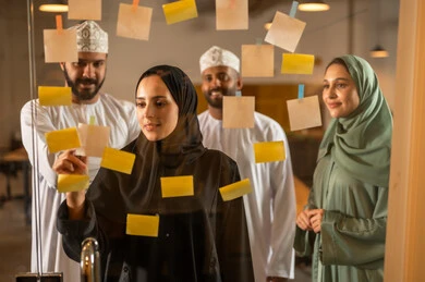 أوراق الملاحظات الملونة المعلقة, بيئة العمل في الشركات العمانية ،كتابة وتدوين شيء ما , مهن وأعمال مكتبية, صورة لمجموعة موظفين عربيين خليجيين عمانيين يقومون  بلصق اوراق  ملاحظة على واجهة زجاجية داخل المكتب