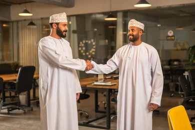 Agreement and partnership on business and commercial projects, acquaintance and friendships, and building social relationships, successful new business deals between businessmen, two Arab Gulf Omanis shaking hands inside the company headquarters with gestures of happiness and joy. Agreement and partnership on business and commercial projects, acquaintance and friendships, and building social relationships, successful new business deals between businessmen, two Arab Gulf Omanis shaking hands insi