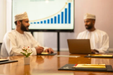 Conducting a job interview, successfully closing new business deals between businessmen, two Omani Arab Gulf men wearing traditional attire discussing their work tasks, expanding business fields, partnership in business and engineering projects, studying statistical data, analyzing charts.